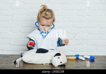 Ragazzo giocare medico con una mucca giocattolo sul muro bianco. Bambino veterinario esamina toy animale con stetoscopio. Futura professione concetto. Salute, healthcare, med Foto Stock