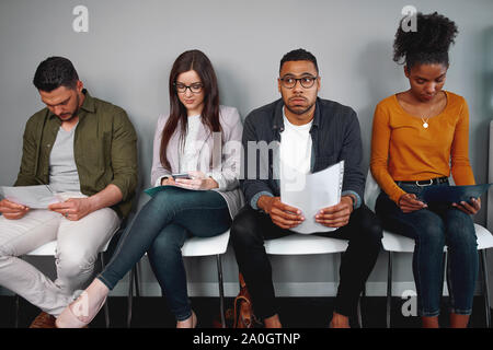 Preoccupata e ha sottolineato l'uomo tenendo la sua riprendere la seduta con altri candidati in attesa per il colloquio di lavoro in ufficio - Diversi giovani gruppo di candidati Foto Stock