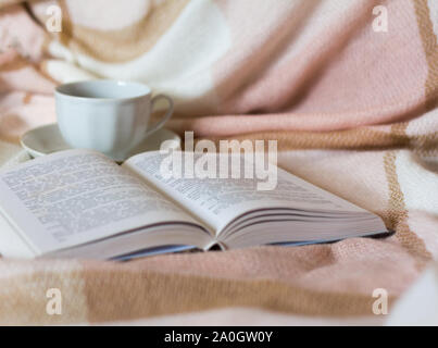 Una tazza di caffè e un libro aperto sullo sfondo di una calda coperta Foto Stock