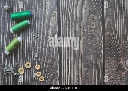 Accessori per il cucito sul legno scuro dello sfondo. Verde filetti di cucitura, ago, i pulsanti e i perni. top view, flatlay Foto Stock