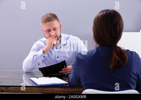Giovane imprenditrice Guardando preoccupato pensieroso imprenditore seduti al colloquio in ufficio Foto Stock