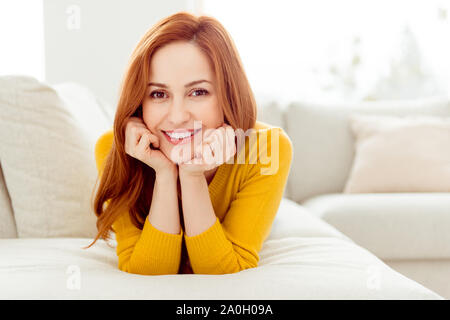 Delicato, winsome, amabile, donna affascinante con i capelli dritti stendo sul lettino accogliente in maglione giallo trascorrere il tempo libero in moderno luminoso bianco inter Foto Stock