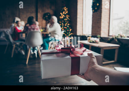 Prospettiva in prima persona Noel famiglia grande raduno della vigilia. Tagliata di close-up dando a mano scatola regalo bianca confezione bow, nastro. Nice grey-haired nonni, chi Foto Stock