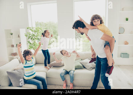 Spensierato, sogno, dolce pre-teen momenti concetto. Ritratto di bel papà e tre bambini sit, saltare il ponticello sul lettino in luce luminoso soggiorno, padre Foto Stock