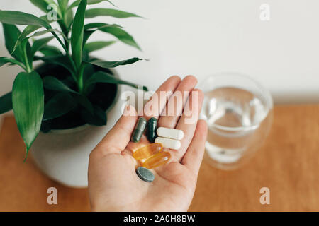 Mano azienda omega 3, spirulina, clorofilla,capsule di magnesio al di sopra di un bicchiere di acqua su un tavolo di legno. Mattina vitamina pillole. Integratori alimentari. Hea Foto Stock