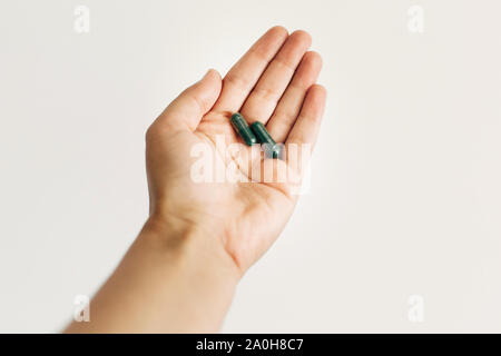 Integratori alimentari. Mano che tiene la spirulina capsule sul muro bianco sullo sfondo. Mattina vitamina pillola di nutrienti. Assistenza sanitaria e di trattamento. Biologici Foto Stock