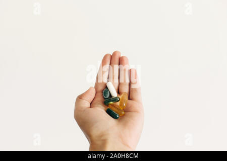 Mano azienda omega 3, spirulina, clorofilla,capsule di magnesio sul muro bianco sullo sfondo. Dose di mattina vitamina pillole. Integratori alimentari. Salute sup Foto Stock