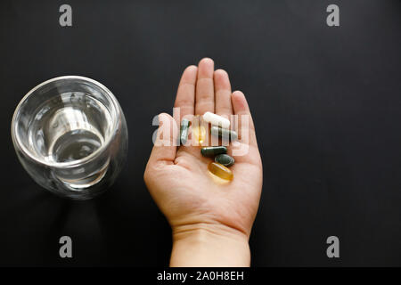 Mano azienda omega 3, spirulina, clorofilla,capsule di magnesio al di sopra di un bicchiere di acqua. Dose mattutina di pillole. Integratori alimentari. Assistenza sanitaria. Bio Foto Stock