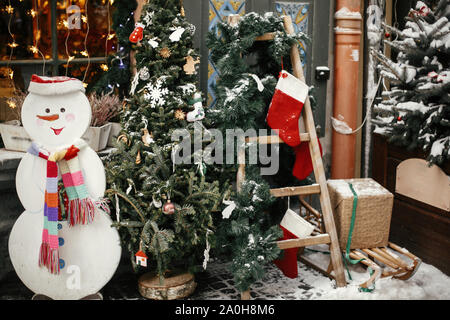 Natale decorazioni di strada. Elegante struttura ad albero di natale con ornamenti festosa, pupazzo di neve e la scaletta con le calze in negozio al mercato per le vacanze in città nevoso stre Foto Stock