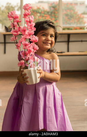 Un simpatico baby in abito rosa azienda fiori di colore rosa Foto Stock