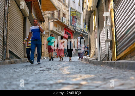 Gruppo di persone a piedi attraverso gli stretti vicoli del quartiere Eminonu di domenica. I negozi sono chiusi, serrande di arresto. Un uomo cammina e parla con il telefono cellulare. Foto Stock