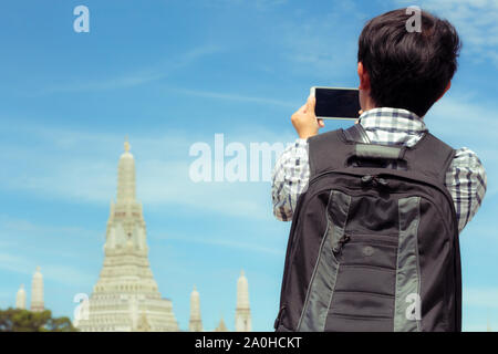 L uomo è selfie permanente sul fiume in Thailandia. I turisti tenendo il telefono cellulare per scattare foto di te sorridente con il Wat Arun in Thailandia. Sono maschio b Foto Stock