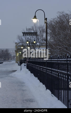 Fila di incandescente luci di strada con ghiaccioli e una recinzione metallica al mattino al crepuscolo in inverno Foto Stock