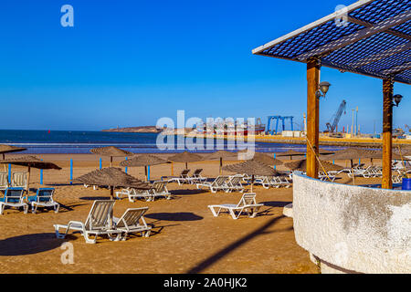 La luce del mattino su una spiaggia deserta con i gabbiani e il porto con colorate barche da pesca in Essaouira, Marocco.il Nord Africa. Foto Stock