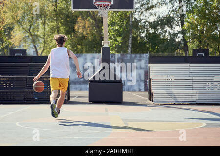 Foto dal retro dell'uomo giocare a basket sul parco giochi sul giorno di estate Foto Stock