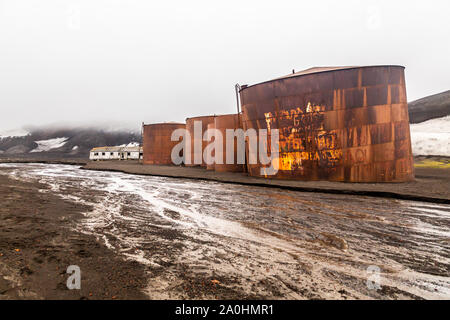 Abbandonata la balena norvegese stazione hunter rusty blubber cisterne con il fiume fangoso in primo piano a isola Deception, Antartico Foto Stock