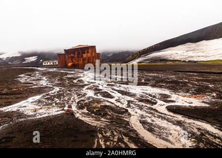 Abbandonata la balena norvegese stazione hunter rusty blubber cisterne con il fiume fangoso in primo piano a isola Deception, Antartico Foto Stock