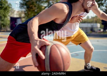 Immagine di giovani atleti giocare a basket sul parco giochi sul giorno di estate contro lo sfondo di verdi alberi Foto Stock