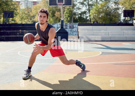 Immagine dell'atleta uomo in blu T-shirt giocare a basket sul parco giochi in estate nel pomeriggio Foto Stock