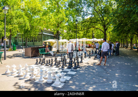 Ginevra, Svizzera - Luglio 19, 2019: persone giocare un esterno di partita a scacchi con gli scacchi giganti di pezzi nel Parc Des Bastions. Scacchi grandi pannelli sono situati all'ingresso del parco nel centro della citta'. Foto Stock