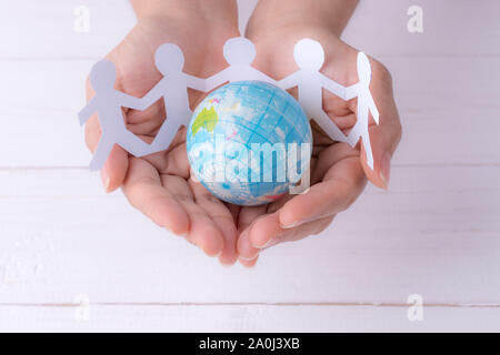 Closeup donna mani globo con gente bianca catena costituita dal taglio della carta. La popolazione mondiale giorno. Foto Stock