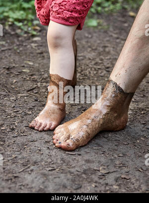 Gli uomini e il bambino presentando vi fangosi piedi su un pavimento di foresta Foto Stock