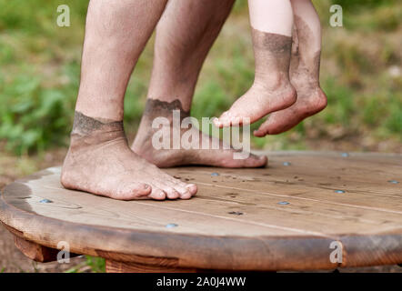 Piedi sporchi di uomini e un bambino su una piattaforma di legno Foto Stock