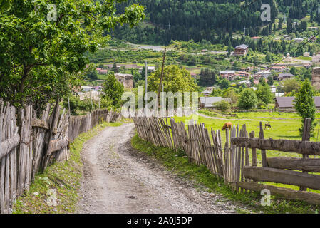Strada sterrata in salita lungo recinti di legno, nella parte superiore di Mestia. Regione di Svaneti, Georgia. Foto Stock
