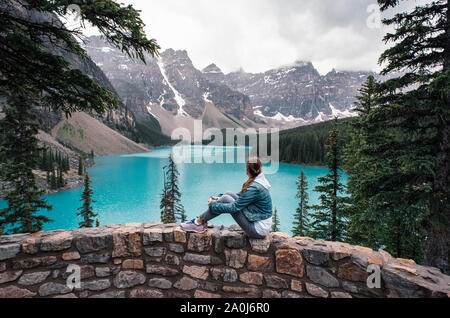 Donna seduta su una parete rocciosa che guarda verso il Lago Moraine e montagne. Foto Stock