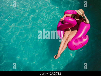 Vista superiore della donna sul galleggiante gonfiabile fenicottero rosa in una piscina. Foto Stock