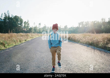 Ritratto di un giovane ragazzo scuola a piedi lungo una strada vuota al tramonto Foto Stock