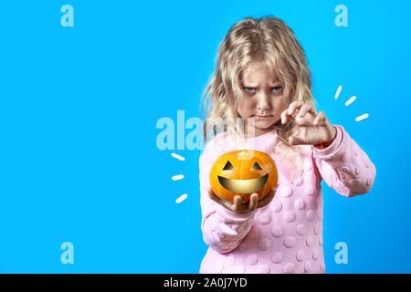 Carino Ragazza strega con capelli biondi evoca oltre una zucca su uno sfondo colorato Foto Stock