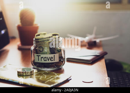 Budget di viaggio concetto. I soldi per il viaggio risparmi in un vasetto di vetro con bussola, passaporto e carta di credito, aereo giocattolo e mappa del mondo sulla scrivania. Foto Stock