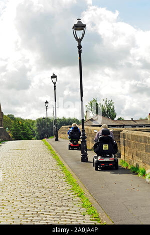 Due persone sulla mobilità scooter sul ponte in pietra con carreggiata in ciottoli di attraversare il fiume Ribble a Preston Foto Stock