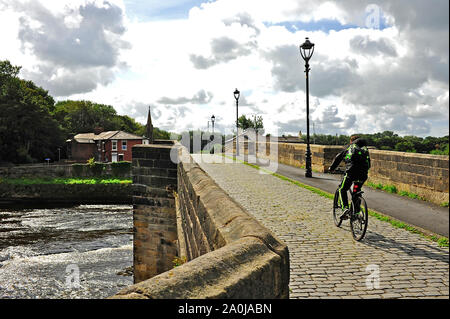 Ciclista sul ponte in pietra con carreggiata in ciottoli di attraversare il fiume Ribble a Preston Foto Stock