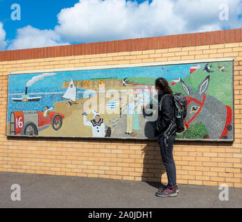 Escursionista femmina guardando il mosaico raffigurante scene di Saltburn. Saltburn dal mare, North Yorkshire, Inghilterra. Regno Unito Foto Stock