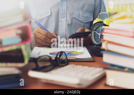 L uomo è utilizzando il telefono cellulare e lavorare con la pila di documenti sulla scrivania in ufficio, imprenditore è analisi di marketing con il grafico delle statistiche, Business e O Foto Stock