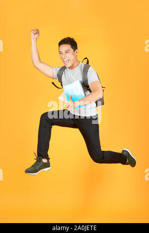 Studente uomo jumping con zaino isolato su sfondo arancione Foto Stock