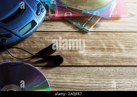 Lettore CD con disco e auricolari su tavola in legno sotto una luce calda Foto Stock
