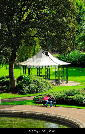 Due persone si sedette sul banco da parte gazebo in Miller Park su una soleggiata giornata estiva Foto Stock