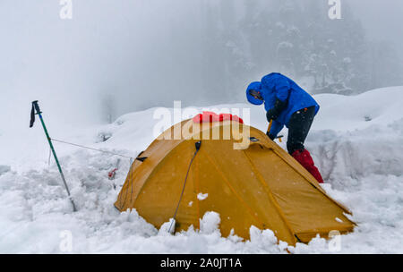 Alpinista lo sgombero neve dalla sua tenda in un pesanti nevicate. Foto Stock