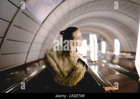 Giovane donna in piedi sulla scala mobile alla stazione della metropolitana Foto Stock