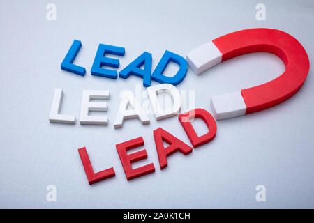 Persona della mano che tiene il magnete a ferro di cavallo per attrarre i fili colorati lettere su sfondo bianco Foto Stock