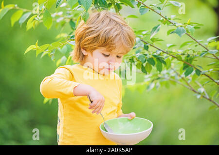 Nutrizione organica. Nutrizione sana nozione. Abitudini alimentari. Kid tenere cucchiaio. Piccolo bambino di gustare pasti fatti in casa. La nutrizione per i bambini. Poco toddler boy porridge di mangiare all'aperto. Avendo grande appetito. Foto Stock