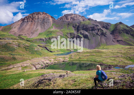 La donna si siede su una roccia ammirando laghetti alpini nel lago ghiacciato bacino superiore in San Juan National Forest, Silverton, Colorado, STATI UNITI D'AMERICA Foto Stock