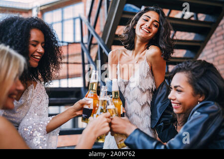 Quattro donne allegro insieme permanente sulla scala tostare le bottiglie di birra Foto Stock