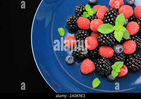 Piastra con fresche Lamponi, more e mirtilli con foglie di menta isolato su sfondo scuro. Vista superiore Foto Stock