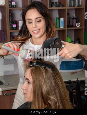 Parrucchiere professionale essiccazione Ragazza capelli lunghi asciugacapelli e il pettine. Processo di styling dei capelli nel salone di bellezza Foto Stock