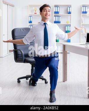 Il giovane imprenditore facendo sport stretching al lavoro Foto Stock