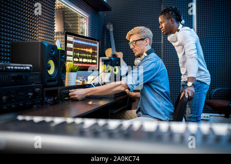 Giovane uomo informale l'aggiunta di volume durante la registrazione di musica con il suo collega africana Foto Stock